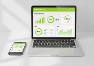 A modern laptop and smartphone displaying a Marketing KPIs dashboard with green data visualizations for ROI, conversion rates, and business growth analytics on a minimalist white desk.
