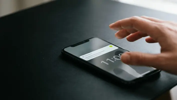 Hand reaching for a phone showing a scheduled post notification beside a clock